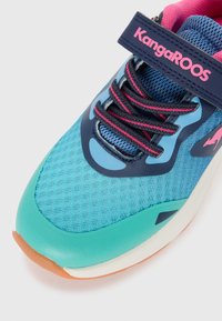 Türkise Sportschuhe mit einem Obermaterial aus Mesh, navyfarbenen Akzenten, pinken Schnürsenkeln und einer Gummisohle mit einem strukturierter Muster für besseren Halt. KangaROOS-Logo sichtbar.