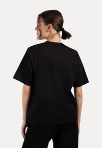 Svart bomullströja med avslappnad passform, korta ärmar och rund halsringning. Tyget verkar mjukt med minimala sömdetaljer.