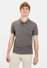 Grijze polo met korte mouwen, kraag en een subtiele logo-patch. Gemaakt van een gladde stof. Draagt bij lichte cargoshorts.