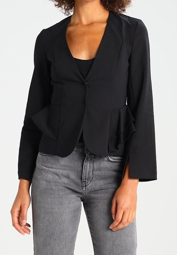 Černý peplum blazer s hlubokým výstřihem do V, dlouhými rukávy a uzávěrem na jeden knoflík; spojený se šedými džíny. Hladká tkanina a přizpůsobený střih.