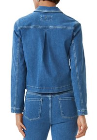 Jeansjacka i mellanblått med en kortad design, långa ärmar och en veck bak. Har sömnadsdetaljer och fickor med lappar.