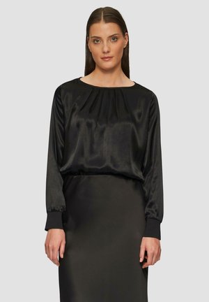 Schwarzes Satin-Top mit runder Ausschnit, geplisster Vorderseite und langen Ärmeln mit elastischen Bündchen. Kombiniert mit einem passenden schwarzen Rock.