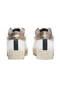 Sneakers bianchi con dettagli metallici dorati e una striscia nera sul tallone. Suola in gomma testurizzata e occhielli per i lacci sono visibili.