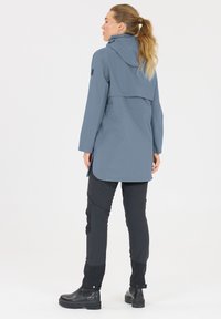 Ljusgrå vattentät jacka med huva, utrustad med en knäppt ståndkrage och en längre bakdel. Matchad med svarta slim-fit byxor och stadiga svarta kängor.