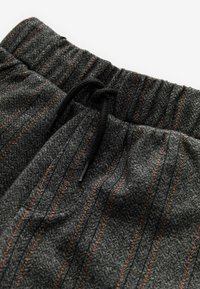 Graue gemusterte Stoffhosen mit dünnen orangefarbenen Streifen, einem elastischen Bund mit Kordelzug und einer strukturierten Oberfläche.