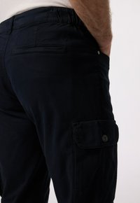 Námořnické cargo kalhoty s elastickým pasem, bočním cargo kapsou a plochou zadní kapsou. Hladká textilie a jemné detaily šití.