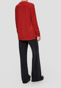Pull long en maille rouge à manches longues avec fentes latérales, associé à un pantalon en denim foncé à taille haute et jambes larges, et des chaussures à plateforme noires.