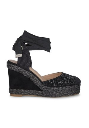 Espadrilla con zeppa nera caratterizzata da una tomaia in tessuto texturizzato, dettagli decorativi con perline e una suola in juta intrecciata. Includerà anche un cinturino alla caviglia regolabile.