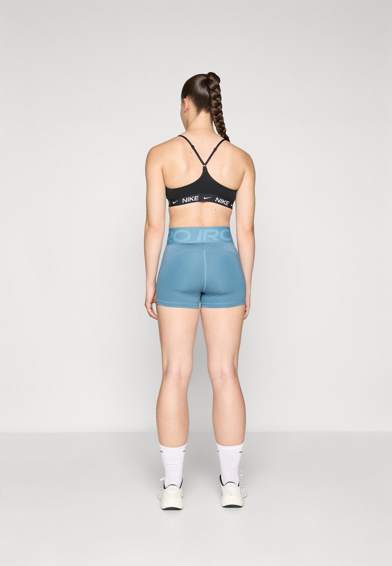 Soutien-gorge de sport noir avec logo Nike blanc, associé à un short taille haute bleu avec une taille couleur bleu clair, modèle de dos.