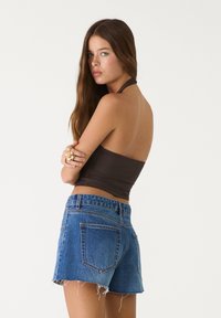 Ruskea halterneck crop-top yhdistettynä sinisiin farkkushortsihin, joissa on revityt helmaukat ja taskuyksityiskohdat, nähtynä takaa.