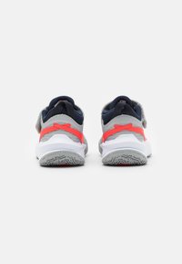 Lasten urheilukengät, joissa on harmaa verkkomateriaali yläosa, tummansiniset yksityiskohdat, kirkkaanpunaiset päällysteet ja valkoinen pohja, jossa on teksturoitu pito.