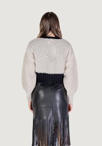 Maglione lavorato a maglia color crema con un orlo a coste nero, abbinato a una gonna in pelle nera con dettagli in frange.