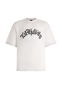 Hvid oversize t-shirt lavet af bomuld med sort "Ed Hardy" tekst trykt i gotisk skrifttype. Udsatte sømme tilføjer detalje til designet.