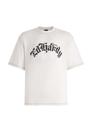 Camiseta blanca de gran tamaño hecha de algodón que presenta texto negro "Ed Hardy" impreso en una fuente gótica. Las costuras expuestas añaden detalle al diseño.