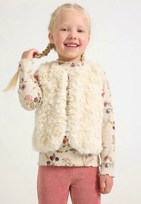 White faux fur vest over a floral long-sleeve shirt, with ribbed pink pants. The vest has a soft, textured surface and no fasteners.