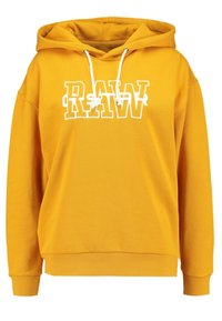 Musztardowa bluza z kapturem z białymi sznurkami i dużym białym napisem "RAW" na piersi, ściągacze przy mankietach i u dołu, luźny krój.