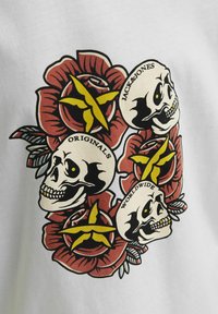 Bílý tričko s grafikou červených růží a lebek, s černými obrysy, žlutými akcenty a textem: "JACK&JONES," "ORIGINALS," "WORLDWIDE."