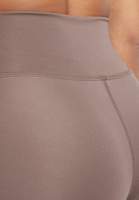 Hoge taille legging in een gedempt bruin, gemaakt van soepel rekbaar materiaal met versterkte stiksels langs de naden.