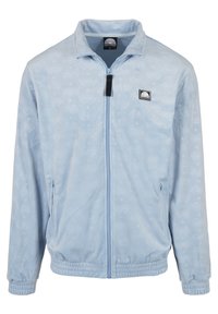 Veste polaire bleu clair à fermeture éclair, avec poignets et ourlet élastiques, poches latérales zippées et écusson noir avec logo sur la poitrine gauche.
