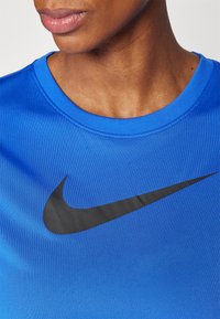 Sininen Nike urheilupaita, jossa on pyöreä kaula-aukko, sileä pinta ja suuri musta swoosh-logo rinnassa.