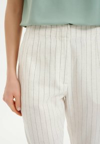Witte linnen broek met verticale marineblauwe strepen, met een hoge taille en een getailleerde pasvorm. De textuur lijkt licht en ademend.