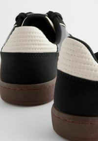 Sneakers neri e crema con un tessuto testurizzato, suola piatta e tacco arrotondato, arricchiti da dettagli di cucitura a contrasto.