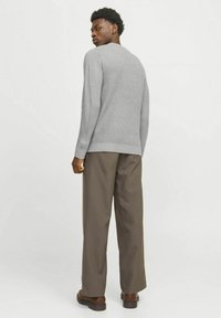 Un suéter gris de punto con un patrón texturizado, cuello redondo y puños ajustados, combinado con unos pantalones marrones sueltos y zapatos oscuros.