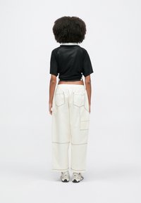 Μαύρο κοντό διχτυωτό τοπ με γιακά, συνδυασμένο με κρεμ παντελόνι φαρδύ στο πόδι με πολλές τσέπες και αντίθετες ραφές.