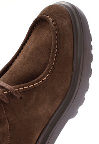 Chaussure en daim marron avec un bout rond, couture contrastante beige, fermeture à lacets et semelle en caoutchouc texturée.