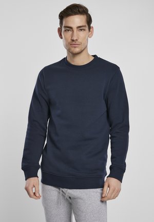 Navyblauer Sweatshirt aus einem weichen Baumwollmix, mit Rundhalsausschnitt, langen Ärmeln sowie gerippten Bündchen und Saum, getragen mit grauen Jogginghosen.