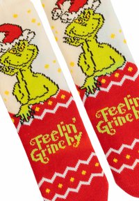 Calze a tema Grinch verdi con un design rosso e bianco, font giocoso con la scritta "Sentirsi Grinchy", arricchite da stelle gialle e motivi a zigzag.