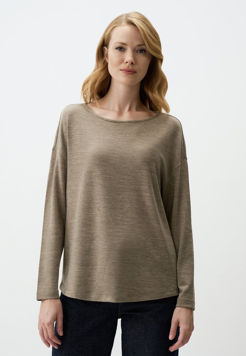 Langärmliges, weiches beiges Oberteil mit einem runden Ausschnitt und lässiger Passform. Glatte Textur und minimale Nahtdetails, kombiniert mit dunklen Jeans.
