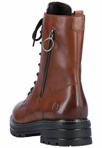Bottine en cuir marron avec un laçage à l'avant, fermeture éclair sur le côté et semelle en caoutchouc. Présente des accents de couture et un détail métallique circulaire.