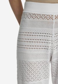 Białe dzianinowe spodnie z teksturowanym wzorem, z naprzemiennymi sekcjami otwartych i zamkniętych oczek, wykończone szerokim elastycznym pasem.