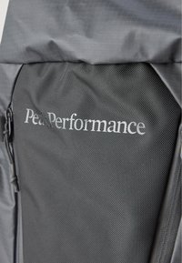 Zaino nero in tessuto testurizzato. Presenta una parte superiore liscia, cerniere e il logo "Peak Performance" ben visibile in argento.