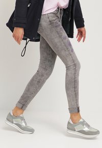 Jeans gris ajustados con un acabado desgastado y un sutil patrón floral. Combinados con zapatillas gris claro con detalles plateados.