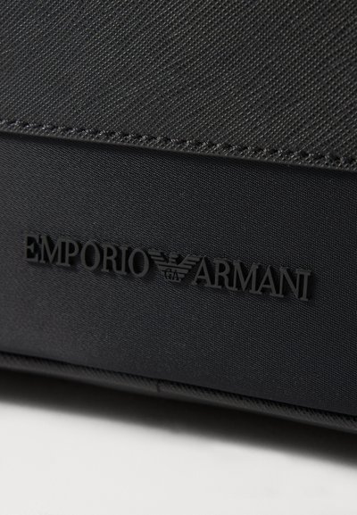 Black textured fabric features an embossed "Emporio Armani" logo on a smooth panel, highlighted by subtle stitching.