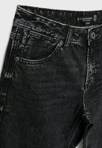 Black denim jeans with a faded finish, featuring front pockets, metal hardware, and stitched detailing along the waistband and seams.