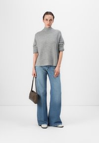 Grå ribbet turtleneck genser, rullede korte ermer, kombinert med lyseblå vide jeans. Modellen holder en brun skulderveske. Svarte og hvite sko.