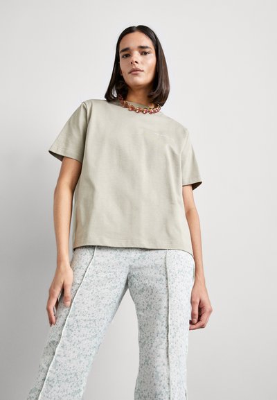 Lichtbeige katoenen t-shirt met korte mouwen, met een eenvoudig ontwerp. Gepaarde met lichtgekleurde broek met bloemmotief en zijsplit.