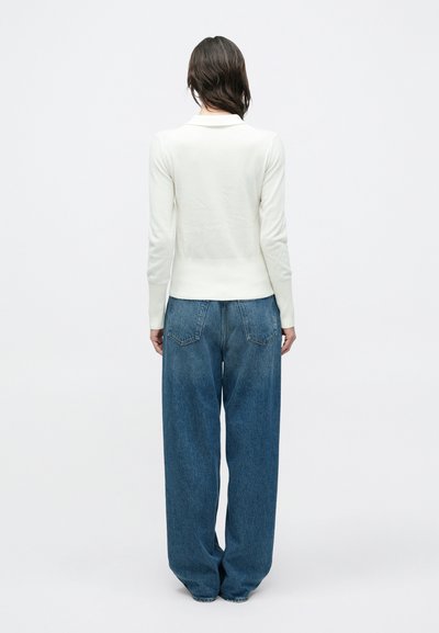 Λευκό πλεκτό τοπ με γιακά, συνδυασμένο με φαρδιά μπλε τζιν παντελόνια. Το σύνολο διαθέτει χαλαρή σιλουέτα και ριμπ λεπτομέρειες στα τελειώματα.