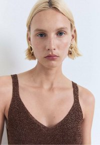 Haut sans manches paillettes marron avec un décolleté en V. Texture lisse, bretelles épaisses, porté avec des boucles d'oreilles en or, arrière-plan neutre.
