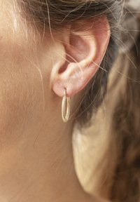 Orecchino ad anello in oro con superficie texturizzata, sospeso dal lobo. Il design presenta una forma circolare sottile con una leggera lucentezza.