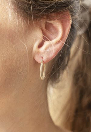 Orecchino ad anello in oro con superficie texturizzata, sospeso dal lobo. Il design presenta una forma circolare sottile con una leggera lucentezza.