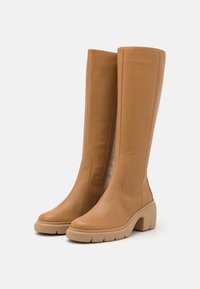 Bottes hautes jusqu'au genou en cuir marron clair avec une texture lisse, un bout arrondi et un talon beige épais. Dotées d'une fermeture éclair latérale pour un enfilage facile.