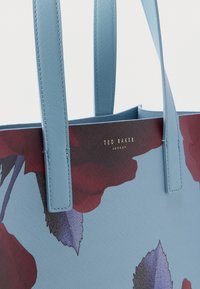 Blue floral print tote bag with textured surface, featuring light blue straps and a gold logo that reads "Ted Baker London."