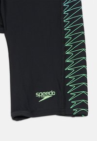Melnas peldbikses, izgatavotas no gludas auduma, ar zaļu zigzaga rakstu sānos un mazu zaļu Speedo logo.