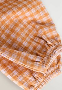 Orange och ljuslila rutigt tyg med mjuk textur, som har ett elastiskt midjeband och skräddarsydda detaljer.