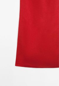 Maglietta rossa in cotone con trama liscia, design semplice e scollo a girocollo. L'orlo è leggermente curvo nella parte inferiore per una vestibilità comoda.