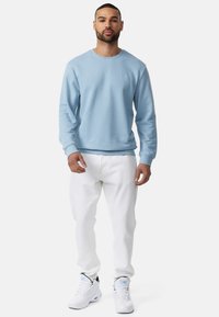 Suéter azul claro de tejido suave, con cuello redondo y puños de canalé, combinado con pantalones blancos y zapatillas blancas con acentos en negro y azul.